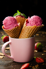 Wafer cones with strawberry icecream in pink mug on wooden kitchen table