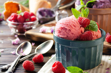 Pink Raspberry icecream balls in clay bowls on wooden kitchen table with berries and spoons aside