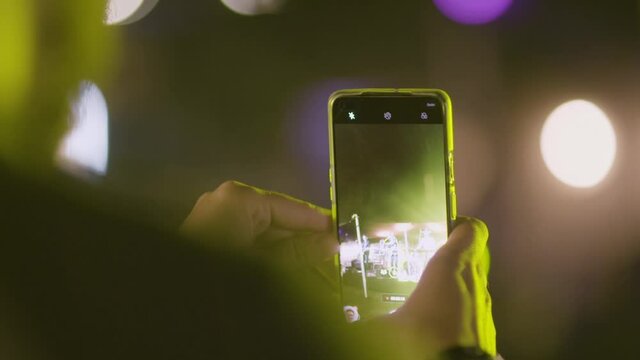 Slow motion close up of a man attending a music concert. Recording the performance on his smart phone