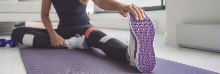 Home workout woman stretching legs on exercise mat before training. Closeup of running shoe banner...