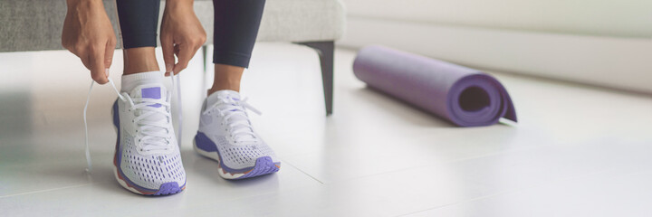 Home workout woman getting ready for training tying her purple running shoes and yoga mat banner...