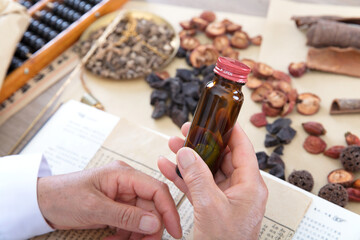 An old Chinese doctor holding a bottle of medicine in his hand view on a table covered with Chinese medicine