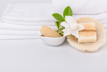 Spa and health care concepts setup with stack of white towels and tropical Gardenia flowers  milk soap luffa scrub on white background