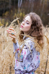 Beautiful girl on a background of a dark forest dry among the herbs. Woman in a dress covered in wheat.