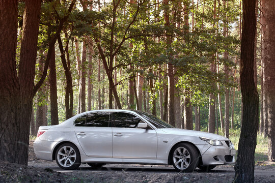 Chernihiv, Ukraine - July 6, 2018: BMW E60 on the forest road. A car with lights on in the forest