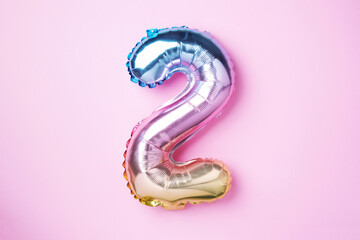 Creative layout. Rainbow foil balloon number and digit two 2. Birthday greeting card. Anniversary concept. Top view. Copy space. Stylish colored numeral over pink background. Numerical digit.