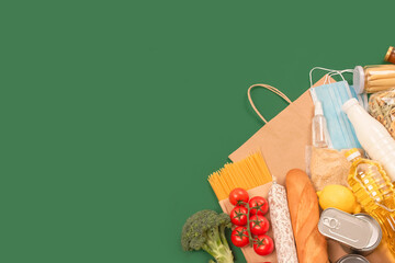 Flat lay composition with food and medicines donations on green background with copyspace - pasta, fresh vegatables, canned food, baguette, cooking oil. Food donations and food bank concept