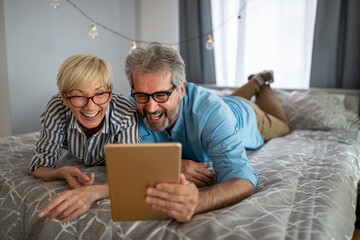 Lovely smiling mature couple having fun while using tablet at home