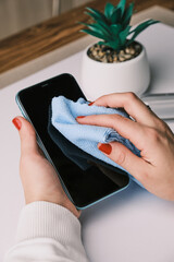Woman Cleaning And Disinfecting Cell Phone Against Virus on a white desk with home plant
