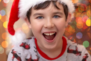 Close-up portrait of a handsome joyful European boy in a red Santa Claus cap