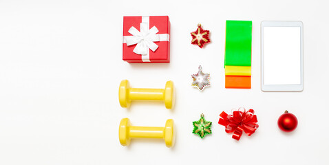 Dumbbells, set of elastic bands, gift box, tablet computer and Christmas decorations on a white background.