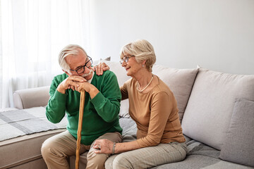Closeup of senior couple hands holding walking stick. Old husband and wife holding cane handle while looking at each other. Happy retired couple joining hands with love at home.