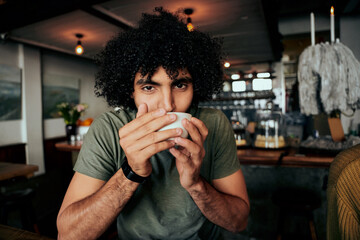 Handsome young man with curly hair sipping hot coffee relaxing in cafe