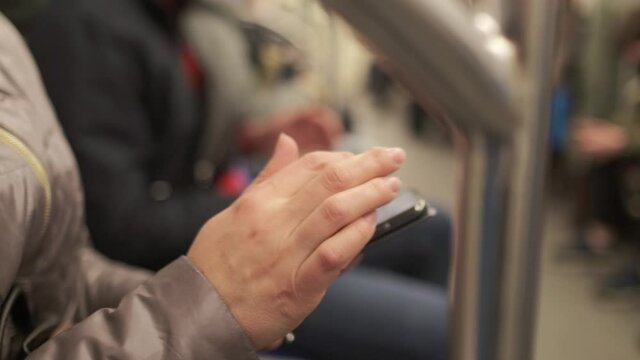 Close-up of female hands in the subway, typing a keyboard on a smartphone, sending a message, looking at photos, communicating on social networks