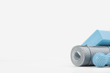 Rolled blue yoga mat and foam block or brick, massage ball. Gender neutral fitness and exercise concept accessories with copy space. Active lifestyle. Workout at home or gym, sports club poster