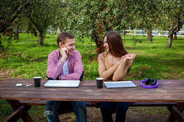 Naklejka premium A guy with a girl working on laptops in the park