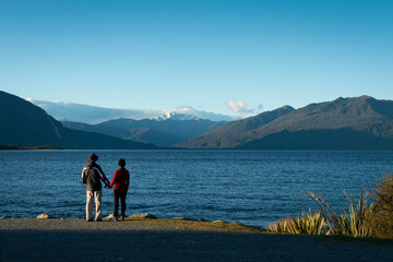 Fototapeta na wymiar Couple enjoying the views of snow-capped mountains at Lake Brunner, South Island, New Zealand