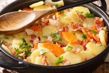 Five-minute potatoes with bacon, onions and carrots close-up in a frying pan on the table. horizontal