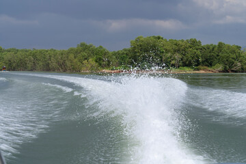 splash water from speed boat motor on ocean with green mangrove forest and rain clouds behind 