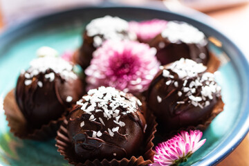 side view, sweet chocolate balls filled with coconut and coconut flakes and garnished with pink flowers, vegan and vegetarian sweets on a blue plate