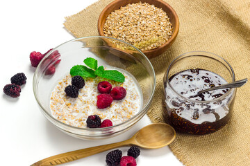 Wheat or spelt flakes porridge in a glass dish with milk and fresh berries on tablecloth isolated on white background. Healthy food concept