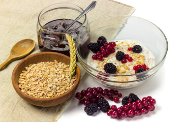Wheat or spelt flakes porridge in a glass dish with milk and fresh berries on tablecloth isolated on white background. Healthy food concept