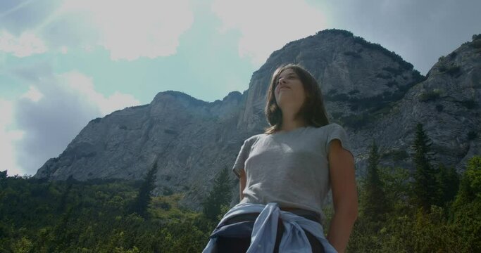 Girl standing proud with mountains and forest behind her, up shot, slow motion
