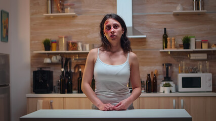 Traumatised woman sitting in the kitchen looking at the camera. Violent aggressive man abusing...