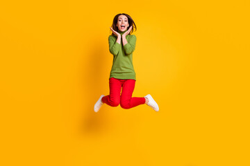 Fototapeta na wymiar Charming crazy lady jump up arms cheeks wear casual green pullover sneakers red trousers isolated yellow color background