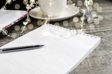 On a wooden table is a Notepad with a pen on the background of a white Cup with bokeh.