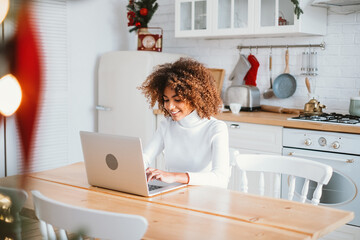 Smiling dark skinned lady in white with short brown kinky hair types on keyboard purchasing online...
