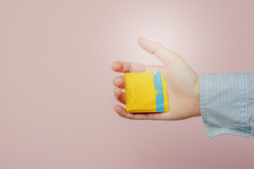 Hand holding a condom isolated on a ping background.Safe sex concept
