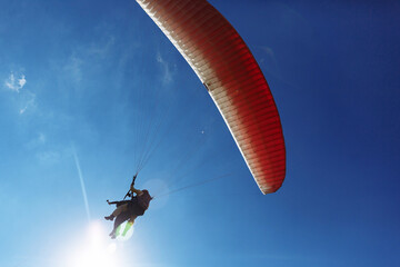 Red paraglider tandem instructor with a tourist flying into the sky with clouds on a sunny day