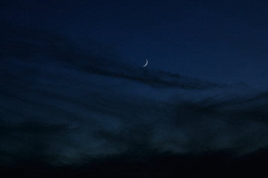 Sickle of the moon in the dark evening clouds. Night photo with the moon and clouds. Moonlight and dark summer clouds.