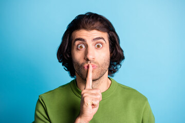 Close up portrait of confused young person show silent sign finger lips green sweater isolated on blue color background