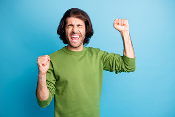 Photo of astonished man closed eyes scream yes fists up wear sweater isolated on blue color...