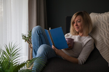 Relaxing woman reading a book and drinking tea at home