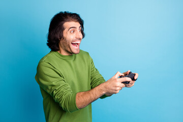 Profile photo of funny bearded guy hold gamepad open mouth wear green pullover isolated blue color...