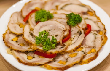 Sliced chicken roll with nut decorated with a sprig of parsley on a white ceramic plate close-up on a tablecloth background