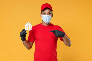 Delivery employee african man in red cap print t-shirt face mask gloves uniform work courier service to home on quarantine coronavirus covid-19 virus concept hold house isolated on yellow background.