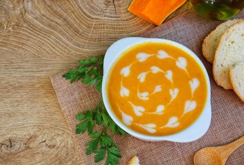 Italian Traditional Pumpkin Soup on top with heart shaped fresh milk served with sliced traditional bread on white bowl with wooden table background.Healthy autumn and winter food