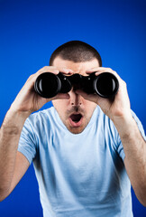 Naklejka premium Man with dark short hair looking through binoculars with a surprised look.