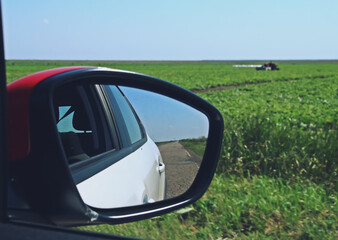 Espejo retrovisor de un coche circulando por una carretera rural. Vista borrosa por efecto de la velocidad de los campos de cultivo del sur de Rumanía.