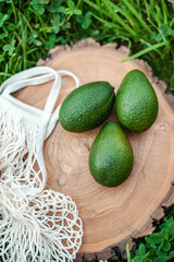 Fresh green avacado on a round wooden board. Eco mesh shopping bag in the frame