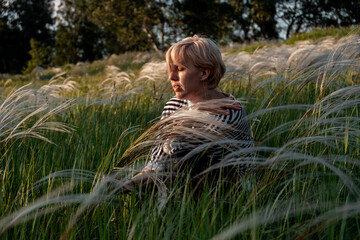 The blonde is resting in the field in the fluffy grass. Unity with nature, travel across the country. Recreation