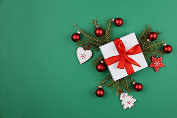 Craft gift box with a red satin bow and spruce branches decorated with Christmas balls, stars on a green background. The festive concept.