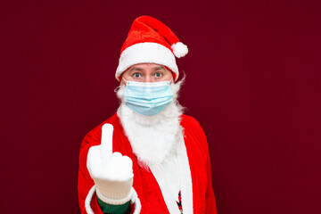 Bad Santa Claus showing the middle finger,he wears a medical mask.Red wall.