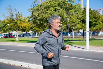 Focused tired mature man jogging outside. Senior jogger training for marathon. Medium shot. Activity and age concept