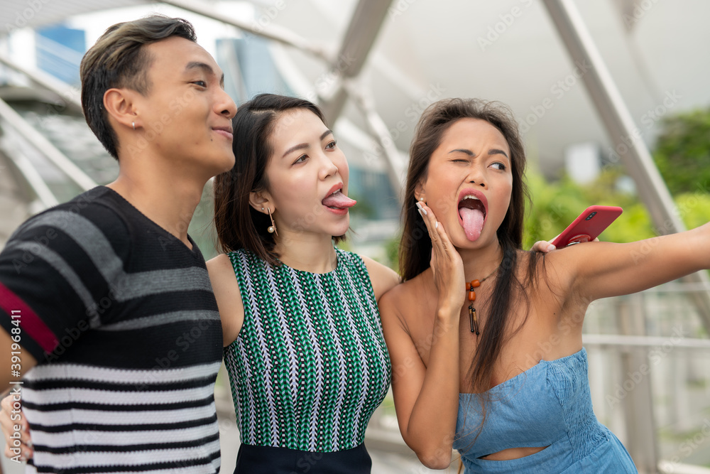 Sticker Three asian young friends outdoor taking selfies. City life of two girls and one boy