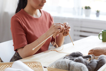 Close-up of young woman using wool for knitting she sitting at the table and doing her work